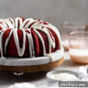 Decadent Fluffy and Moist Red Velvet Bundt Cake 6 A thick cream cheese frosting drizzled on a red velvet bundt cake with pink cups in the background
