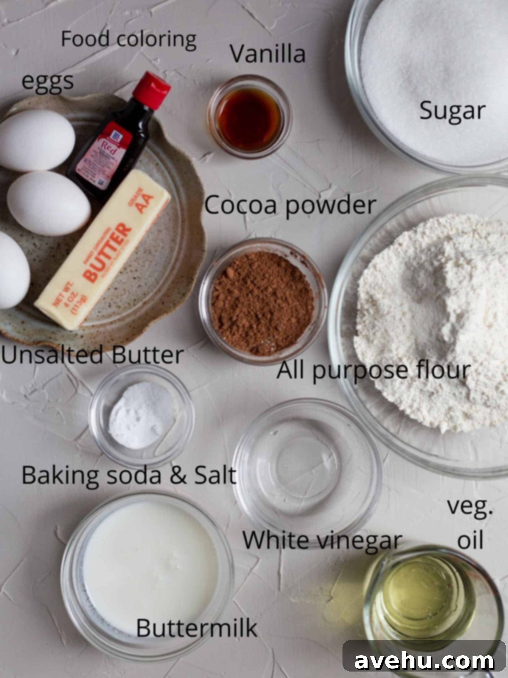 Decadent Fluffy and Moist Red Velvet Bundt Cake 3 A collection of fresh ingredients laid out for making a homemade red velvet bundt cake, including butter, sugar, eggs, buttermilk, flour, cocoa powder, and red food coloring, on a clean kitchen counter.