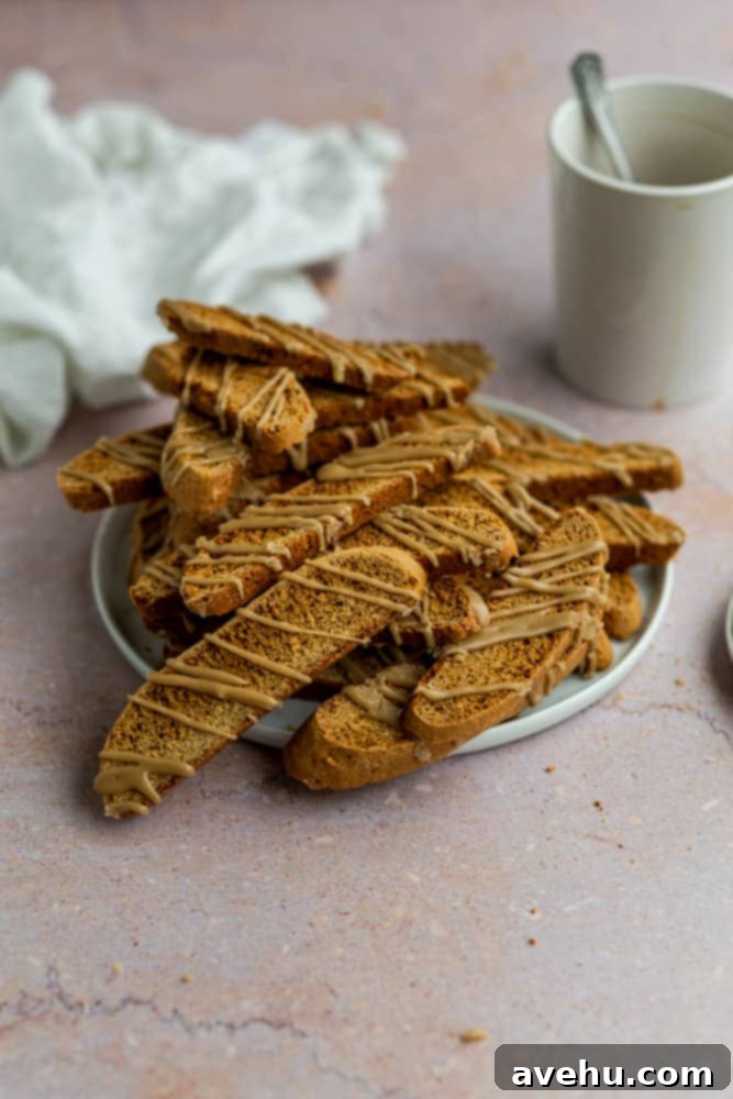 Gingerbread Biscotti with a Frosty Crunch 2 Gingerbread biscotti piled on top of a white plate on a pink background, showcasing their golden color and sweet glaze.