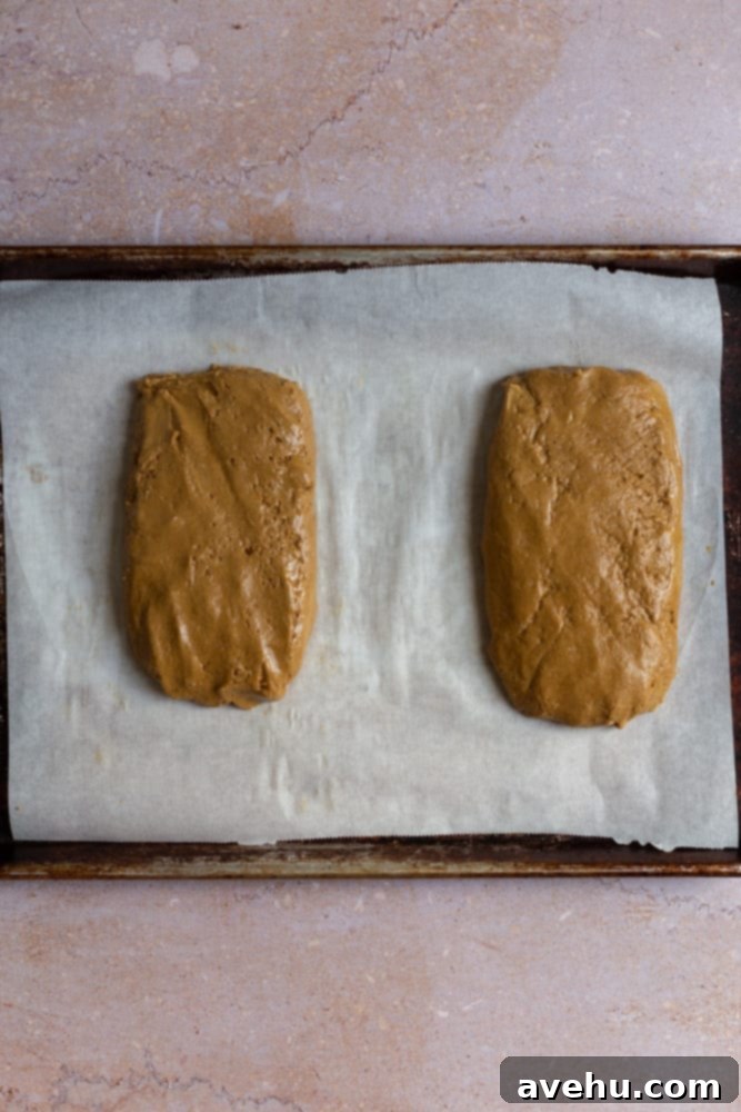 Gingerbread Biscotti with a Frosty Crunch 6 Two unbaked logs of gingerbread biscotti dough on a parchment-lined sheet tray, shaped and ready for the first bake.