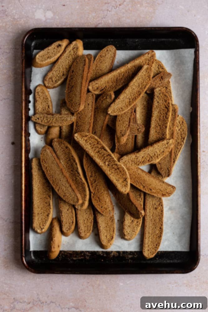 Gingerbread Biscotti with a Frosty Crunch 9 Biscotti cookies piled onto a baking tray lined with parchment paper, arranged for their second bake.