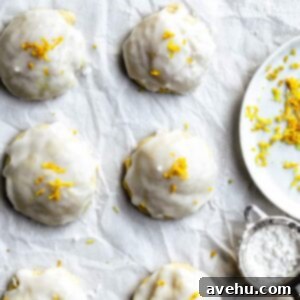 Close up on Italian ricotta cookies with lemon zest next to a plate, showcasing their soft texture and delicate glaze.