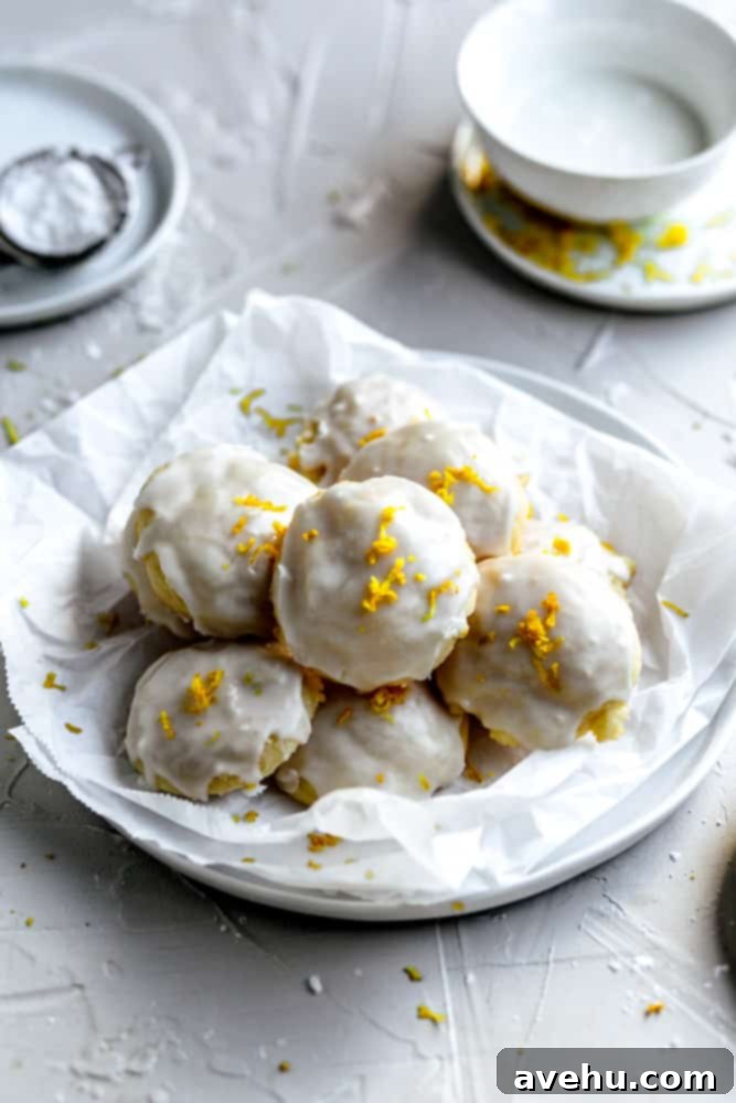 Cloud-Soft Italian Ricotta Cookies 12 A bowl filled with numerous glazed Italian ricotta cookies, some topped with sprinkles and others with lemon zest, nestled on parchment paper for easy serving.