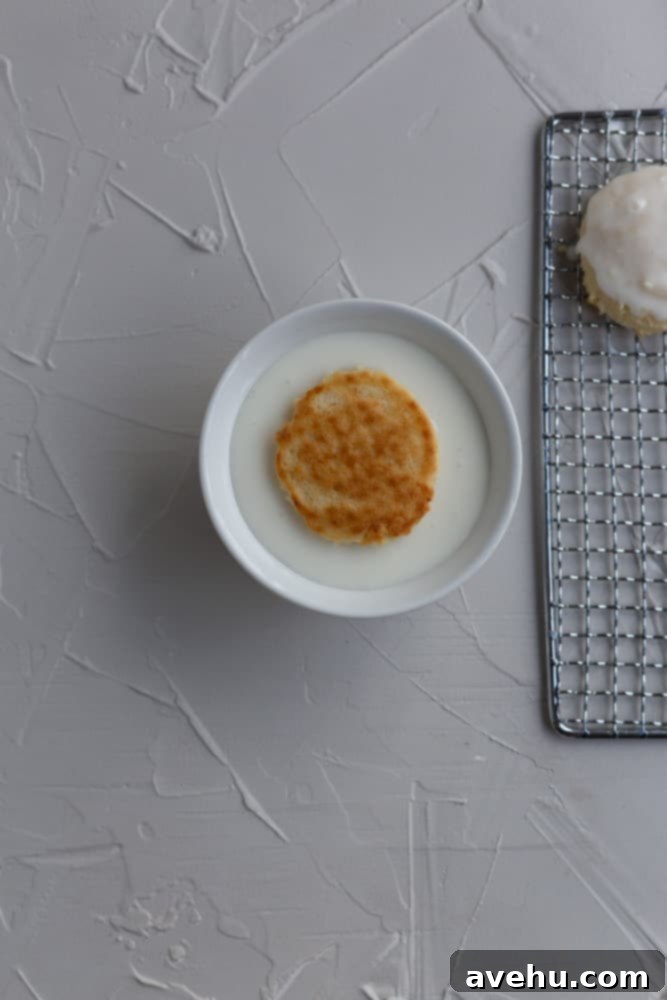 Cloud-Soft Italian Ricotta Cookies 8 A baked Italian ricotta cookie being gently dunked into a small white bowl of smooth, vanilla glaze, capturing the moment before topping.