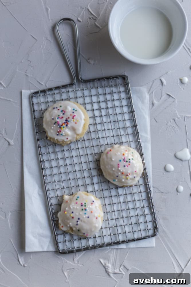 Cloud-Soft Italian Ricotta Cookies 9 Three perfectly glazed Italian ricotta cookies, adorned with colorful sprinkles, sitting on a small wire cooling rack, showcasing their fluffy texture.