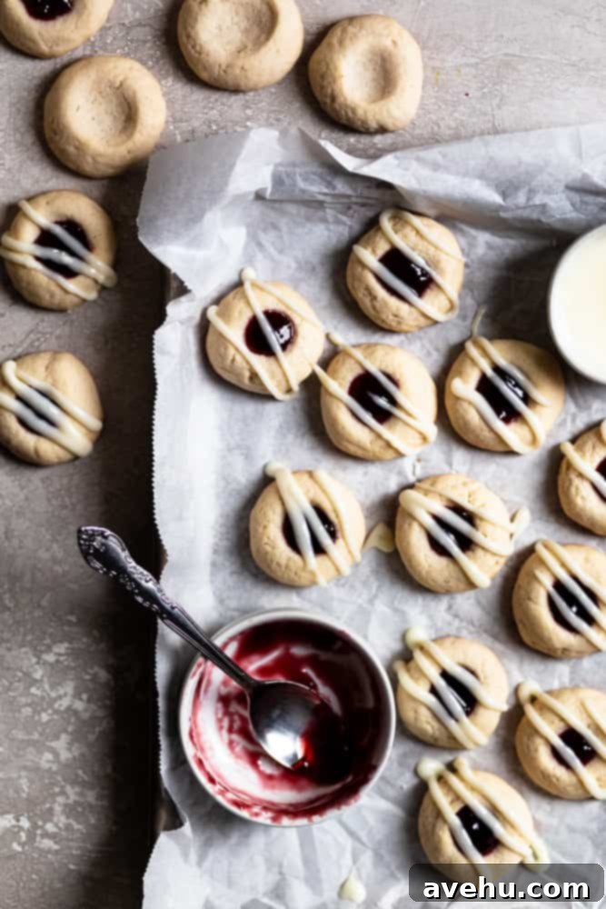 Creamy Raspberry Thumbprint Delights 2 Freshly baked raspberry thumbprint cookies with cream cheese glaze on a parchment-lined cookie sheet, ready to be enjoyed.