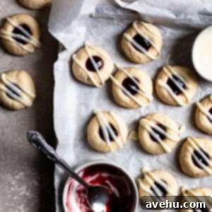 Creamy Raspberry Thumbprint Delights 11 Raspberry thumbprint cookies on a parchment lined cookie sheet