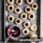 Creamy Raspberry Thumbprint Delights 15 Thumbprint cookies filled with jam on a cookie sheet