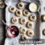 Creamy Raspberry Thumbprint Delights 16 Glazed Raspberry thumbprint cookies on a parchment lined baking tray next to a bowl of jam