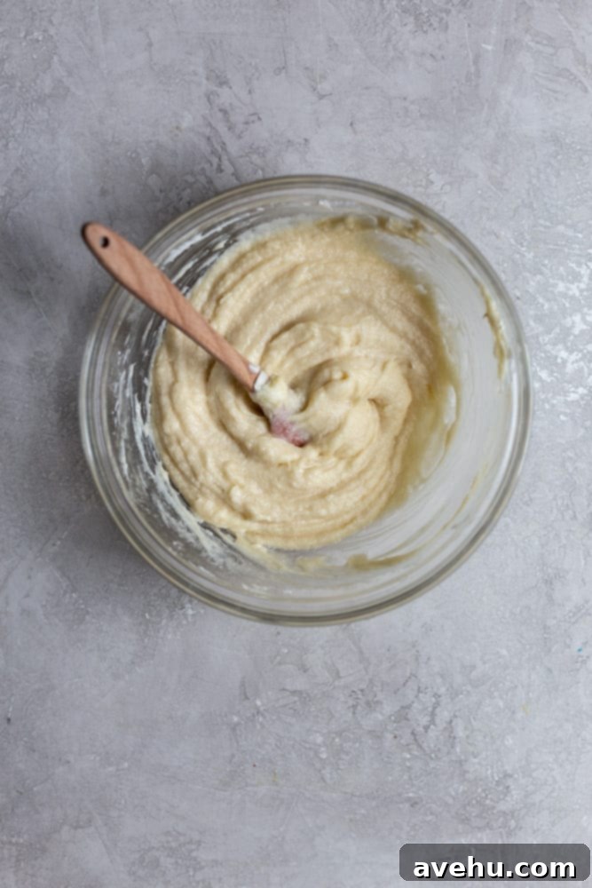 Creamy Raspberry Thumbprint Delights 4 Close-up of butter and sugar being creamed together in a glass mixing bowl on a gray kitchen counter.