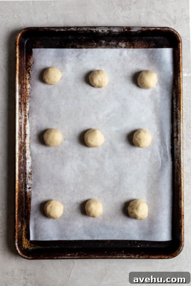 Creamy Raspberry Thumbprint Delights 6 Neatly rolled cookie dough balls arranged on a parchment-covered baking sheet, perfectly spaced.