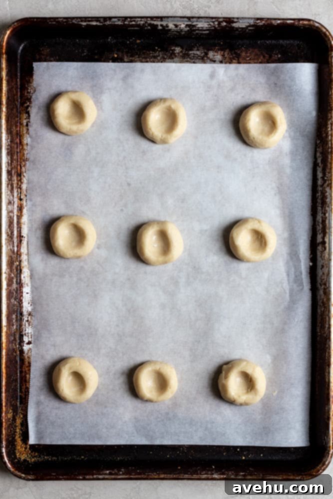Creamy Raspberry Thumbprint Delights 7 Close-up of thumbprint cookie dough balls with perfect indentations on a parchment-lined baking sheet.