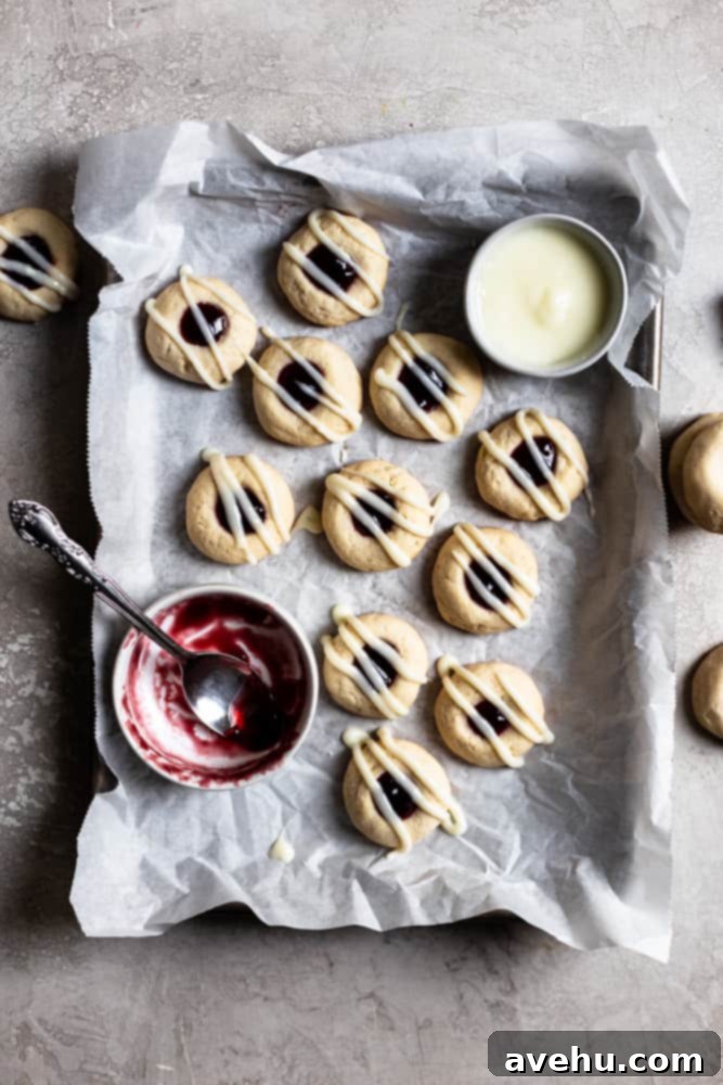 Creamy Raspberry Thumbprint Delights 9 Beautifully glazed raspberry thumbprint cookies arranged on a parchment-lined baking tray, with a small bowl of jam nearby.