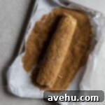Cloudlike Cranberry Shortbread Delights 14 A chilled log of cookie dough being generously rolled in turbinado sugar on a rimmed baking sheet.
