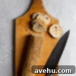 Cloudlike Cranberry Shortbread Delights 15 A log of sugar-coated cookie dough positioned on a wooden cutting board, ready to be sliced with a sharp knife.