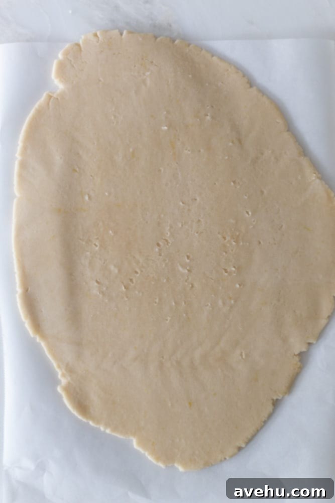 Cloud-Soft Lemon Shortbread 6 Shortbread dough rolled out evenly between two sheets of parchment paper on a white surface