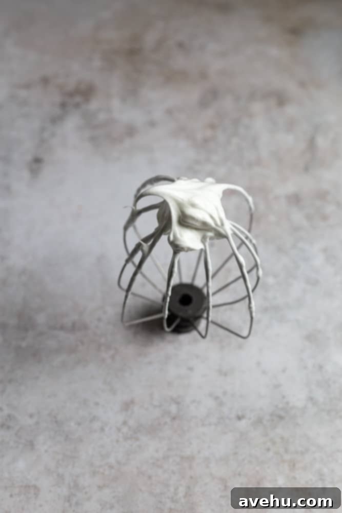 Zesty Lemon Curd Clouds 3 Stiff peaks of meringue on a whip attachment on a gray background