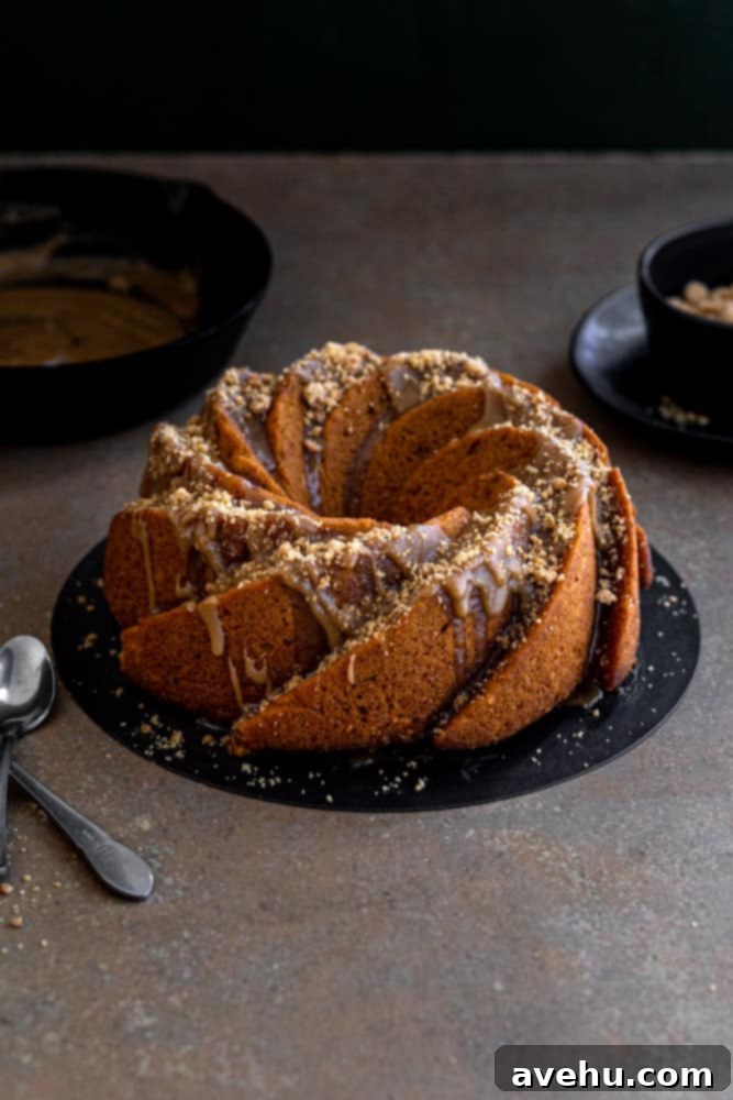 Foolproof Moist Carrot Bundt 2 Beautifully glazed carrot bundt cake on a black cake plate, presented on a rustic dark beige surface. The cake showcases its intricate bundt pan design and the delicious brown sugar glaze dripping down its sides. It's a perfect nut-free holiday cake.