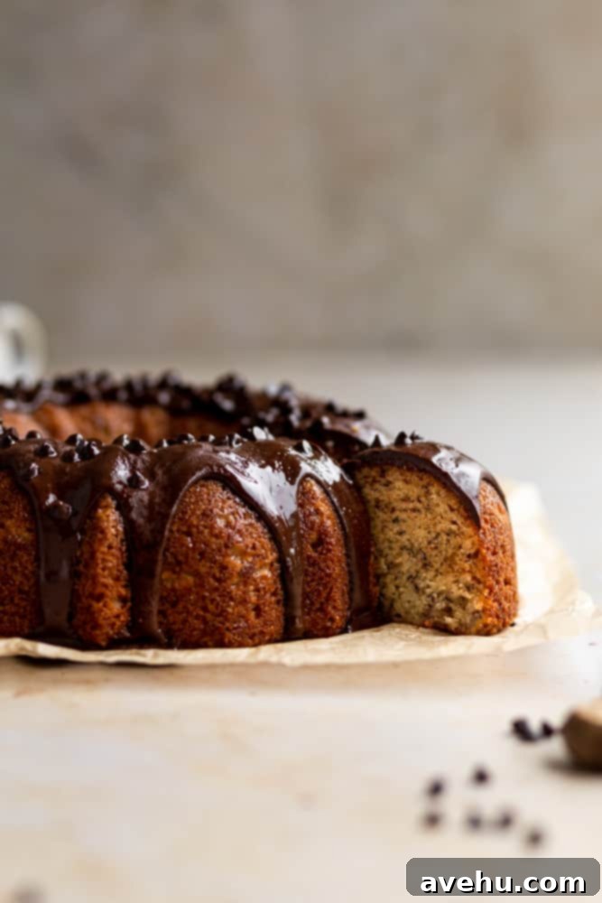 Deliciously Easy Banana Bundt Cake 6 A slice of moist banana bundt cake pulled out from the rest of the cake, with chocolate glaze visible, on a gray surface.