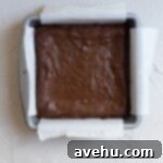 Baked brownies in a parchment-lined 8x8 inch pan, ready to be cooled and cut.