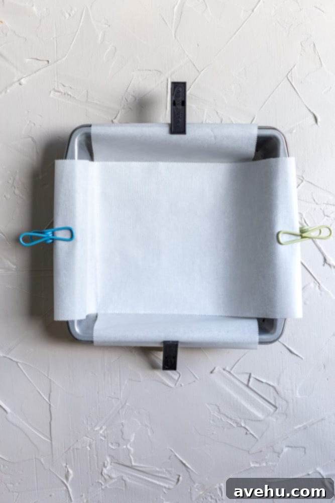 Decadent 30-Minute One-Bowl Fudgy Brownies 4 An empty 8x8 inch square baking pan precisely lined with parchment paper, held in place by small metal clips on the edges