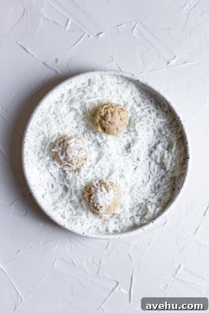 Golden Coconut Delights 4 A ball of cookie dough being rolled in a bowl of shredded coconut.