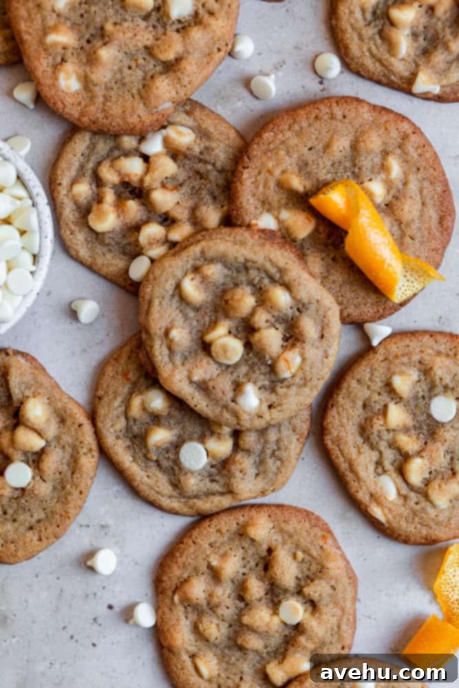 Zesty Orange Crunch-Chews 2 Freshly baked orange cookies with white chocolate chips displayed on a stylish gray surface, ready to be enjoyed.