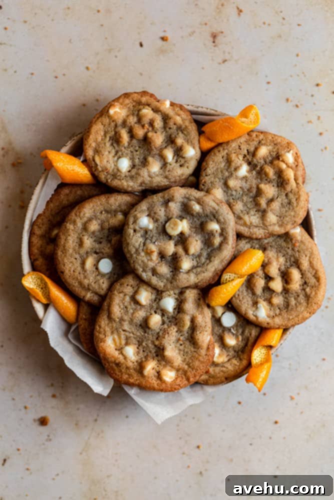 Zesty Orange Crunch-Chews 7 A bowl filled with freshly baked orange cookies, adorned with white chocolate chips, resting on a rustic beige surface.