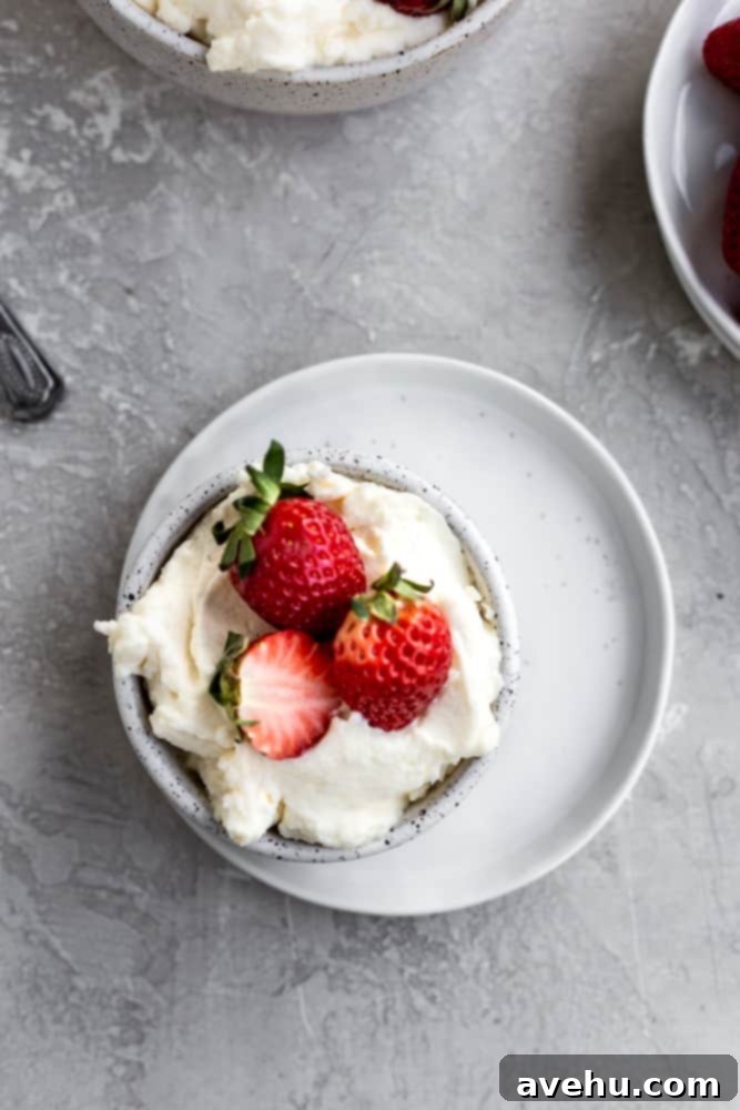 Indulgent Mascarpone Frosting: 10-Minute Perfection 2 A creamy bowl of whipped mascarpone frosting, garnished with fresh, vibrant strawberries, sits on a pristine white plate, promising a delightful dessert experience. This image highlights the smooth texture and appealing presentation of the homemade frosting.