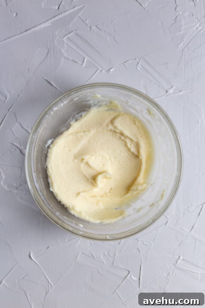 Indulgent Mascarpone Frosting: 10-Minute Perfection 4 A close-up shot of a creamy mascarpone, vanilla, and confectioners sugar mixture being whipped in a clear glass bowl, showcasing its smooth texture and readiness for the next step.