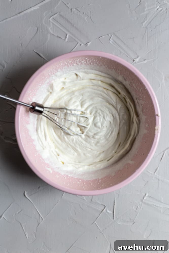 Indulgent Mascarpone Frosting: 10-Minute Perfection 5 Freshly whipped heavy cream with stiff peaks, ready to be folded into the mascarpone mixture. The cream is in a vibrant pink bowl against a textured background, highlighting its airy and stable consistency.