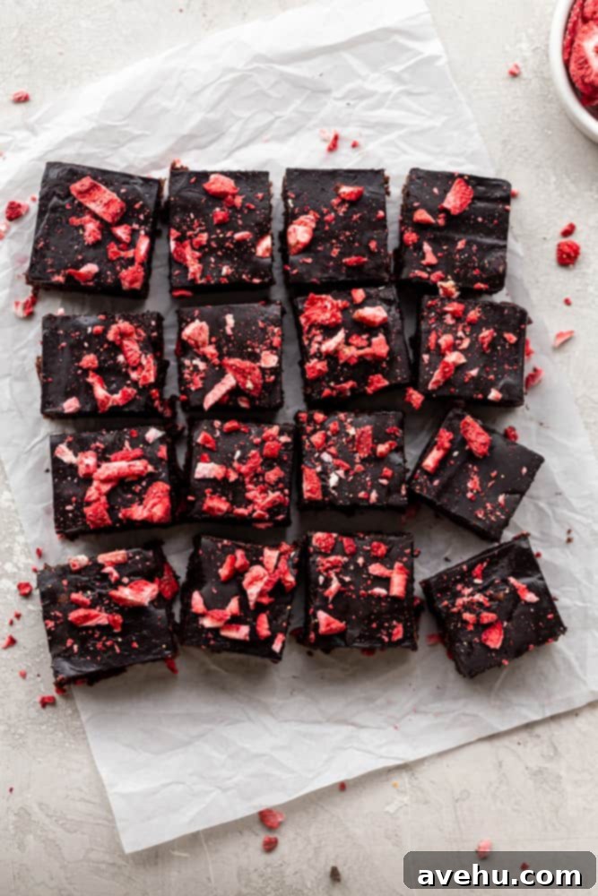 Quick Strawberry Fudge Brownies 9 Several squares of rich chocolate strawberry brownies, topped with smooth ganache and freeze-dried strawberry pieces, arranged neatly on parchment paper