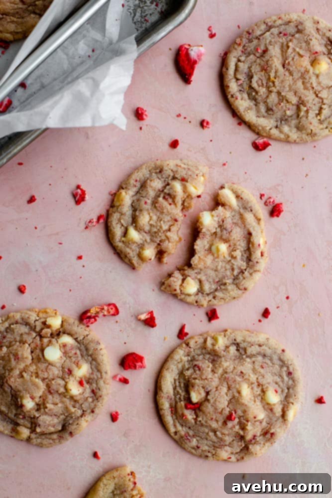 Decadent Strawberry Chewies 2 Freshly baked strawberry cookies broken apart, revealing a soft, pink interior with white chocolate chunks, resting on a vibrant pink surface.