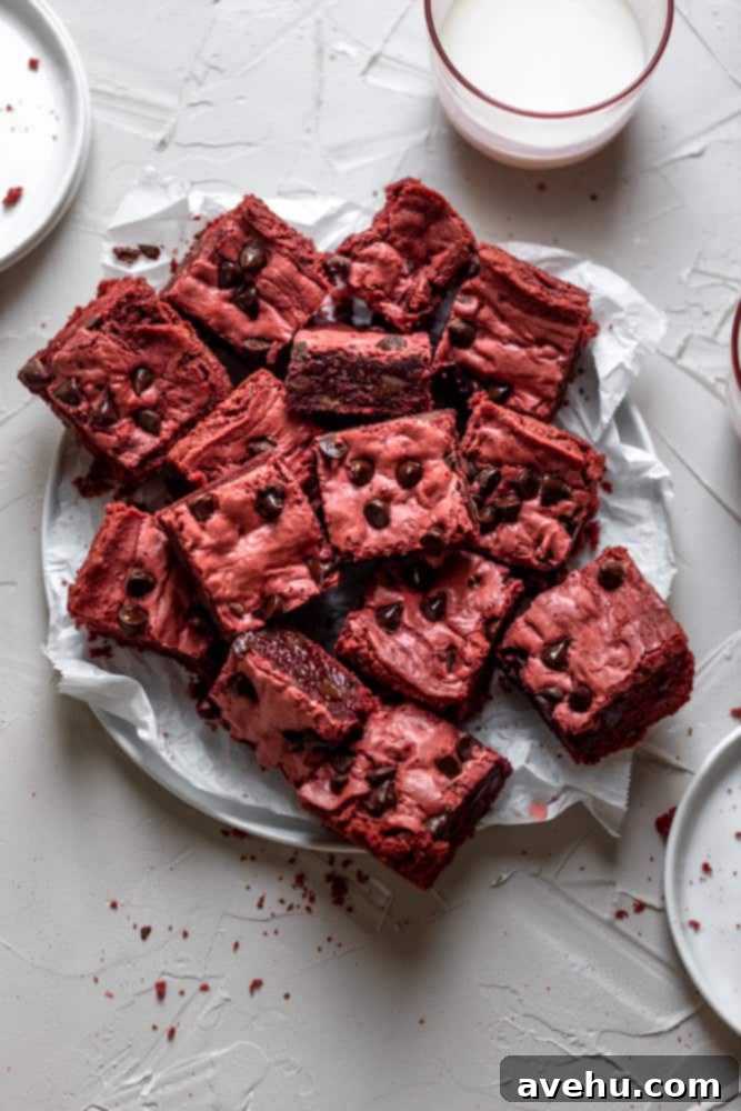Simply Decadent Red Velvet Brownies 2 Red velvet brownies layered on a plate covered in parchment paper, showcasing their fudgy texture and classic red color