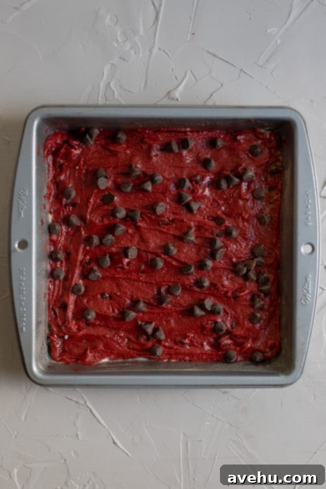 Simply Decadent Red Velvet Brownies 5 Red velvet brownie batter in a baking pan topped with chocolate chips, ready for baking