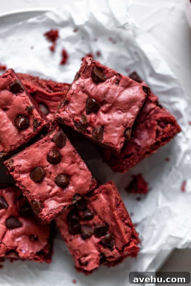Simply Decadent Red Velvet Brownies 6 4 Red velvet brownies layered on top of each other on a piece of crinkled parchment paper, showcasing their rich color and fudgy texture