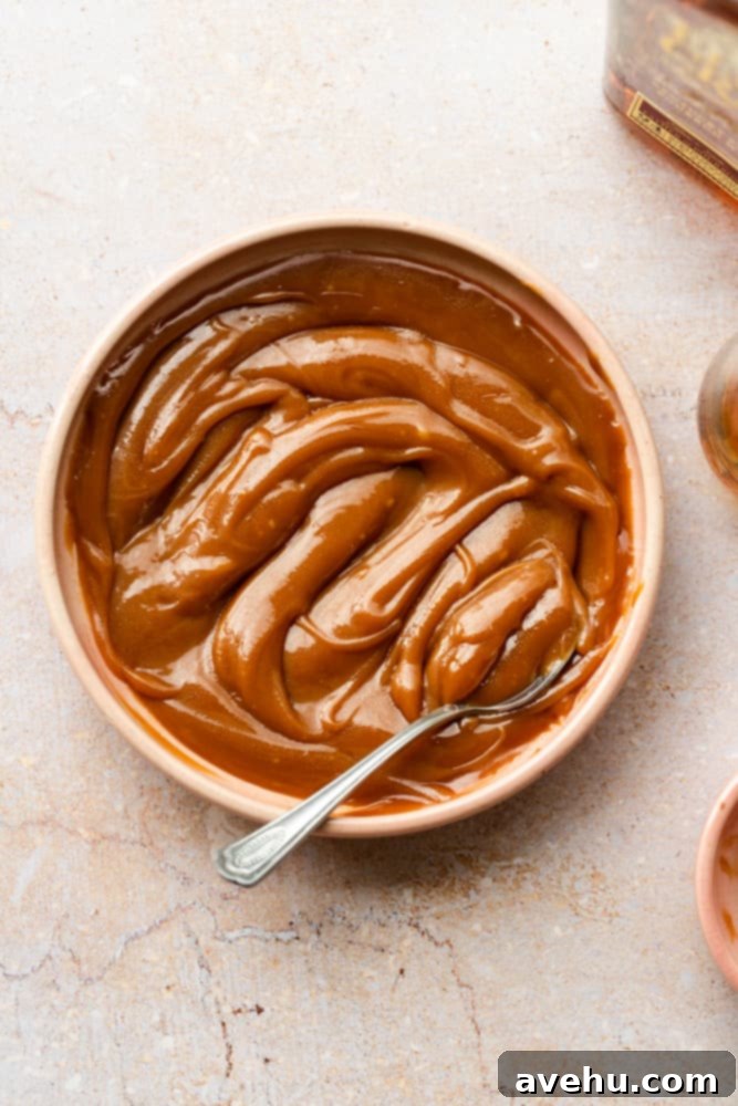 Foolproof Bourbon Caramel Sauce Visual Guide 11 A charming pink bowl filled with rich, homemade bourbon caramel sauce, with a small spoon delicately resting inside, inviting you to taste or drizzle.