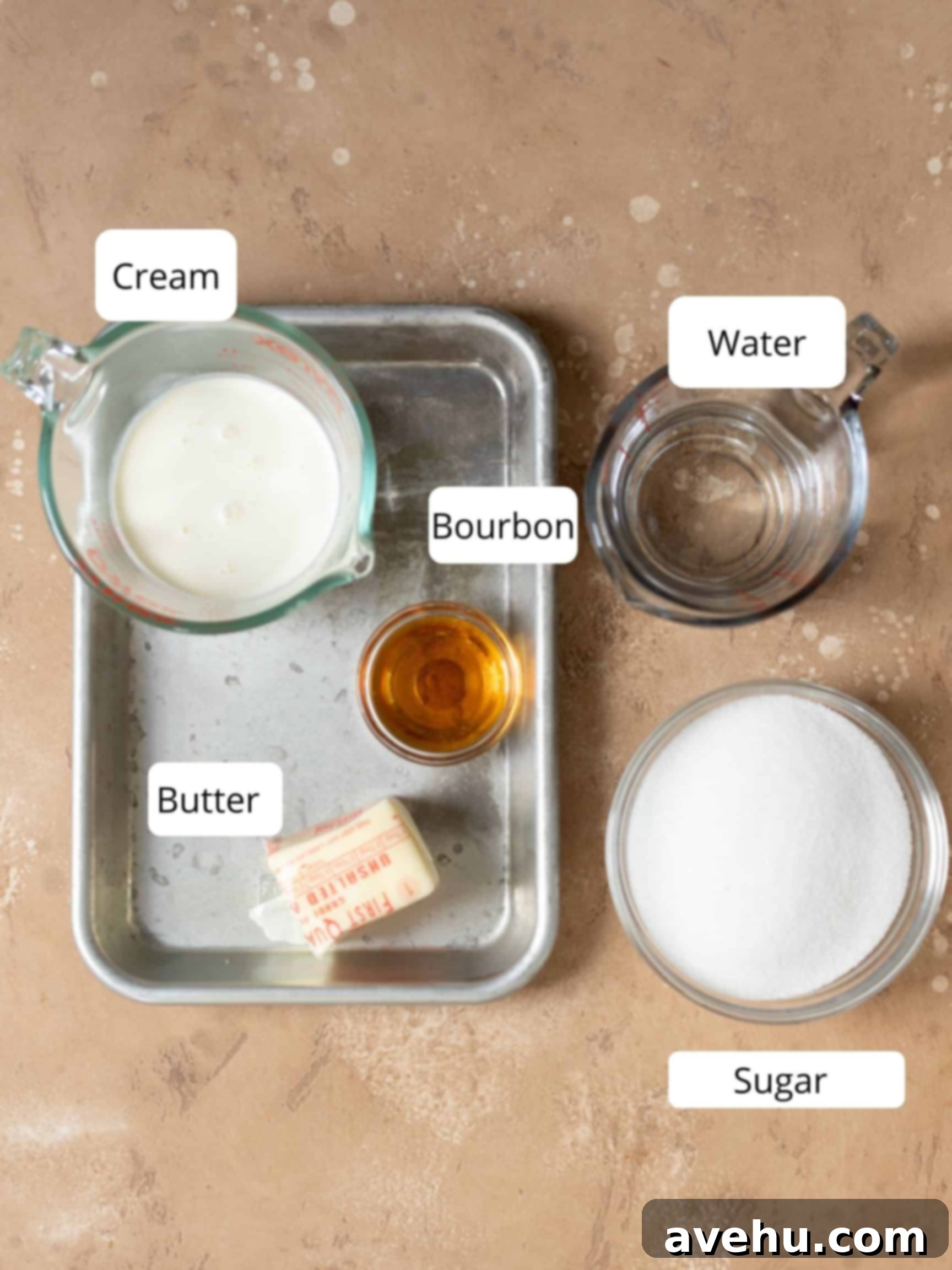 Foolproof Bourbon Caramel Sauce Visual Guide 3 An organized display of ingredients for homemade bourbon caramel sauce, including granulated sugar, water, heavy cream, unsalted butter, a bottle of bourbon, and a small dish of salt, all arranged on a clean kitchen counter.