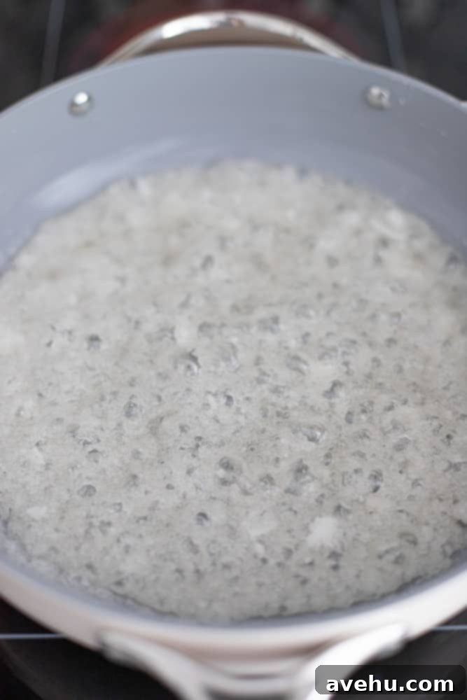 Foolproof Bourbon Caramel Sauce Visual Guide 6 The sugar mixture in the pot showing larger, more vigorous bubbles and hints of yellow, indicating active heating and the start of caramelization.