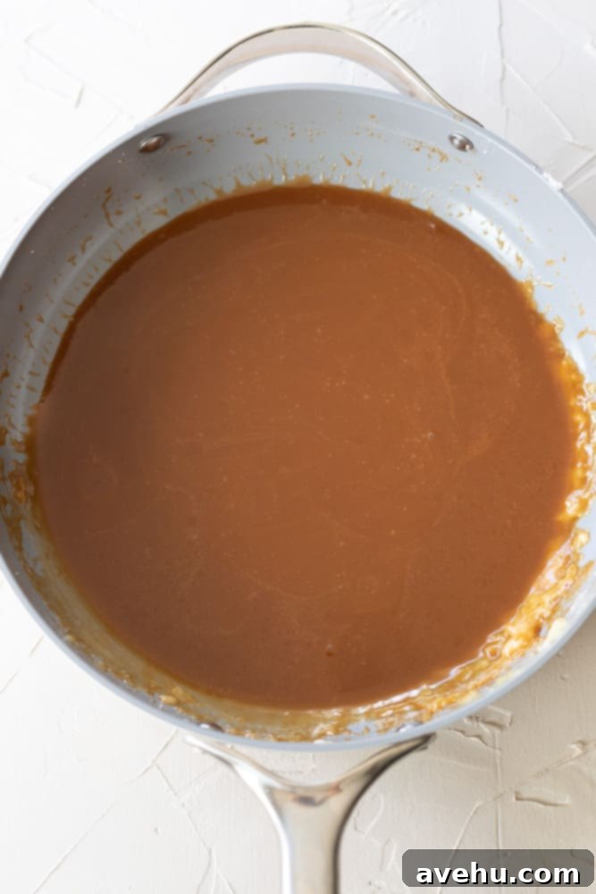 Foolproof Bourbon Caramel Sauce Visual Guide 10 Freshly prepared homemade bourbon caramel sauce, with its rich amber color and smooth, pourable consistency, cooling in a light gray pan on a pristine white surface.