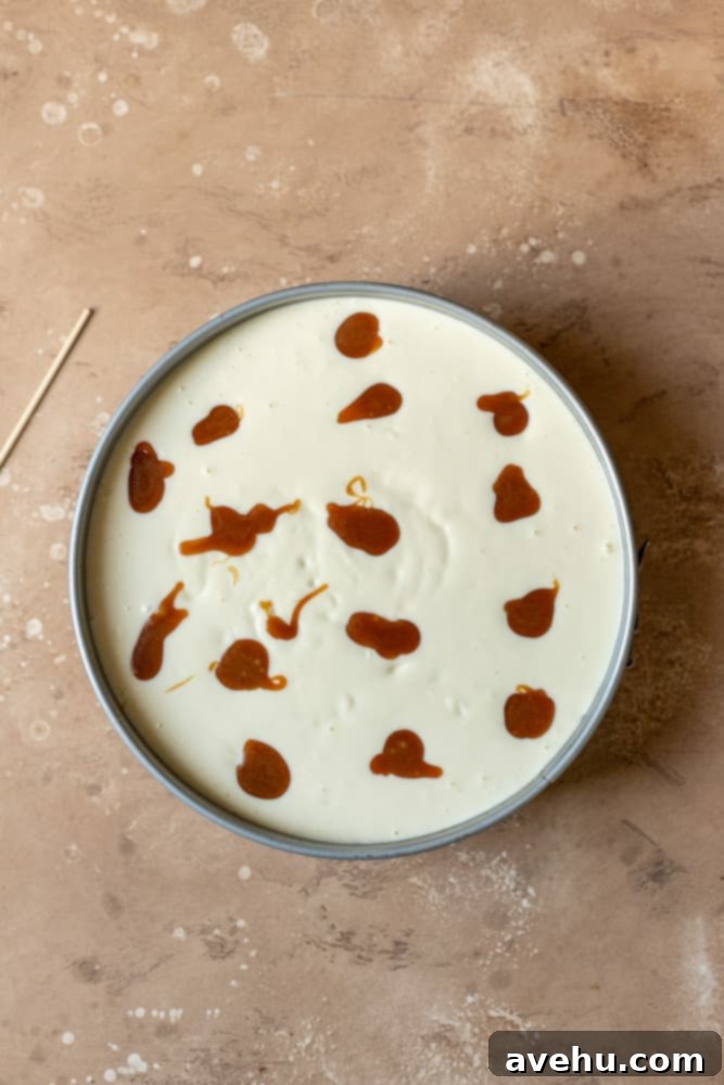 Salted Caramel Cheesecake 7 Cheesecake batter in a springform pan with dollops of rich caramel sauce artfully placed on top, ready for swirling.
