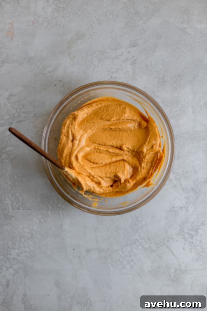 Simple Creamy Pumpkin Mousse Egg Free 4 A pumpkin, cream cheese, and sour cream mixture in a clear glass bowl, showcasing its smooth, creamy texture before whipping.