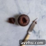 A chocolate cupcake with a hole on it's top with a knife next to it on a blue surface