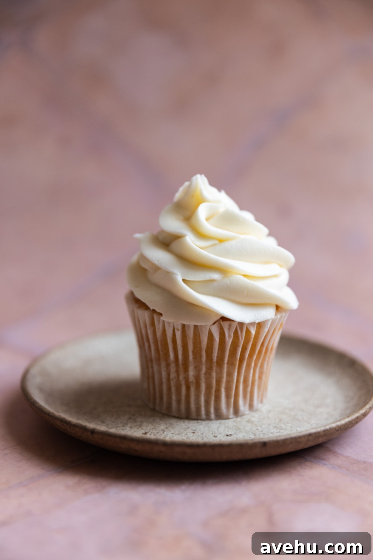 Effortless Pipeable Cream Cheese Frosting 2 A vanilla cupcake with fluffy, stable cream cheese frosting on a stone plate, ready for serving.