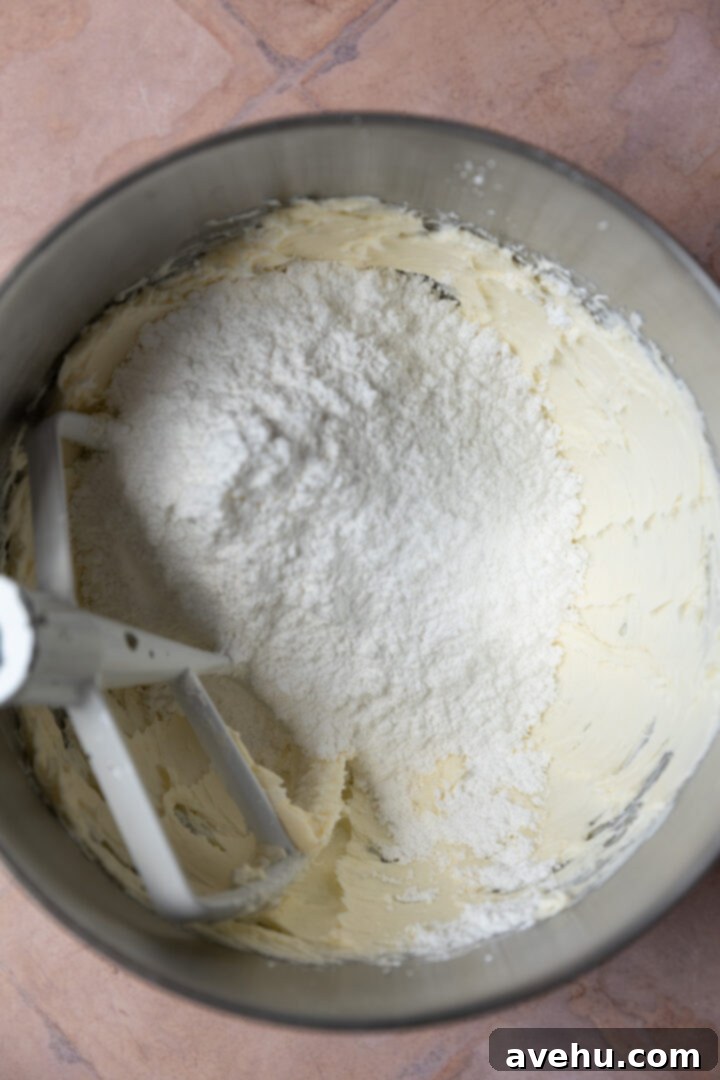 Effortless Pipeable Cream Cheese Frosting 5 Powdered sugar being added to the creamed butter and cream cheese mixture.