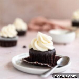 A chocolate cupcake with vanilla frosting on a white plate with a spoon next to it.