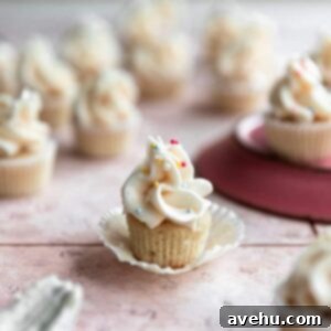 24 Quick Vanilla Mini Cupcakes 2 One mini vanilla cupcake with its liner peeled back on a pink surface, highlighting its moist crumb.
