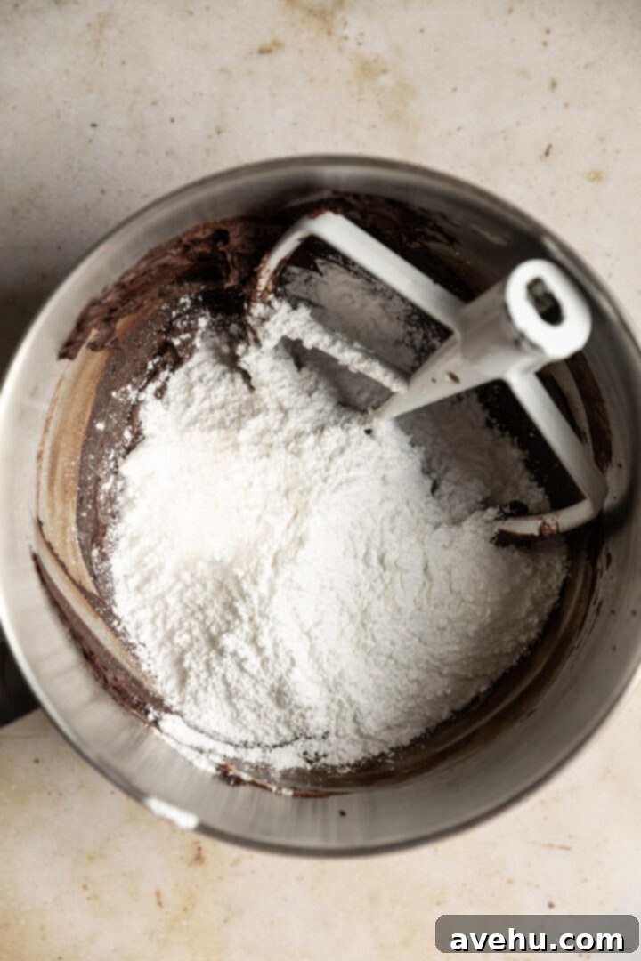 5-Minute Cocoa Chocolate Buttercream Frosting 5 Powdered sugar being added to the creamed butter and cocoa powder mixture in a mixing bowl, preparing for the next step of frosting creation.