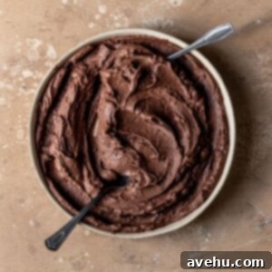 A bowl of rich chocolate buttercream, artfully swirled with two small spoons, invitingly displayed.