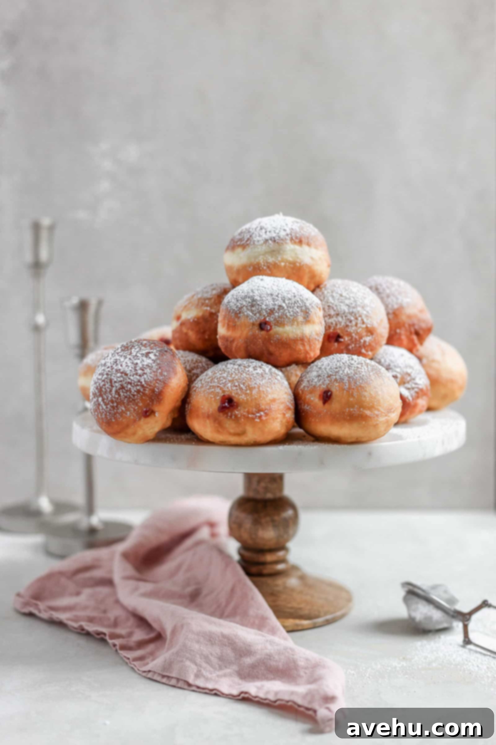 Pillowy Hanukkah Jelly Donuts 2 Chanukah jelly donuts arranged on a cake stand with candlestick in the background.